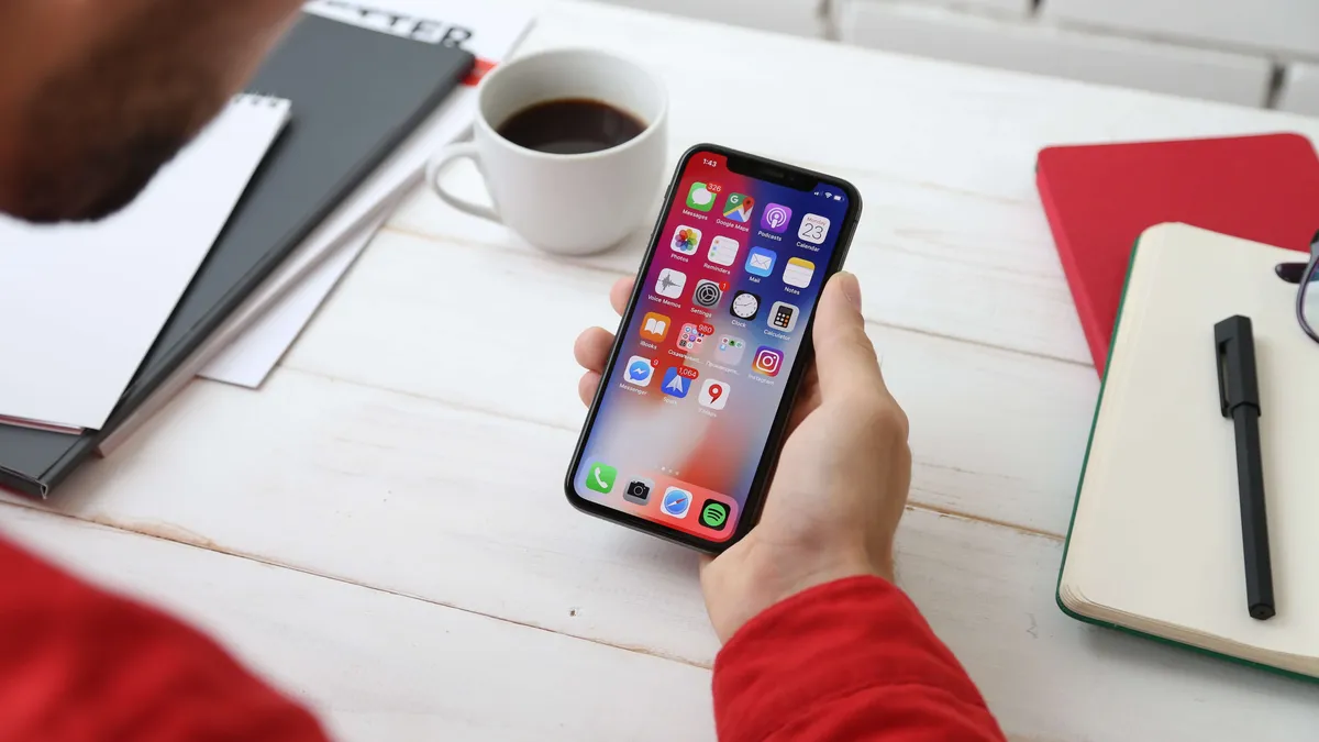 A designer at a desk holding a phone beside a notebook and coffee